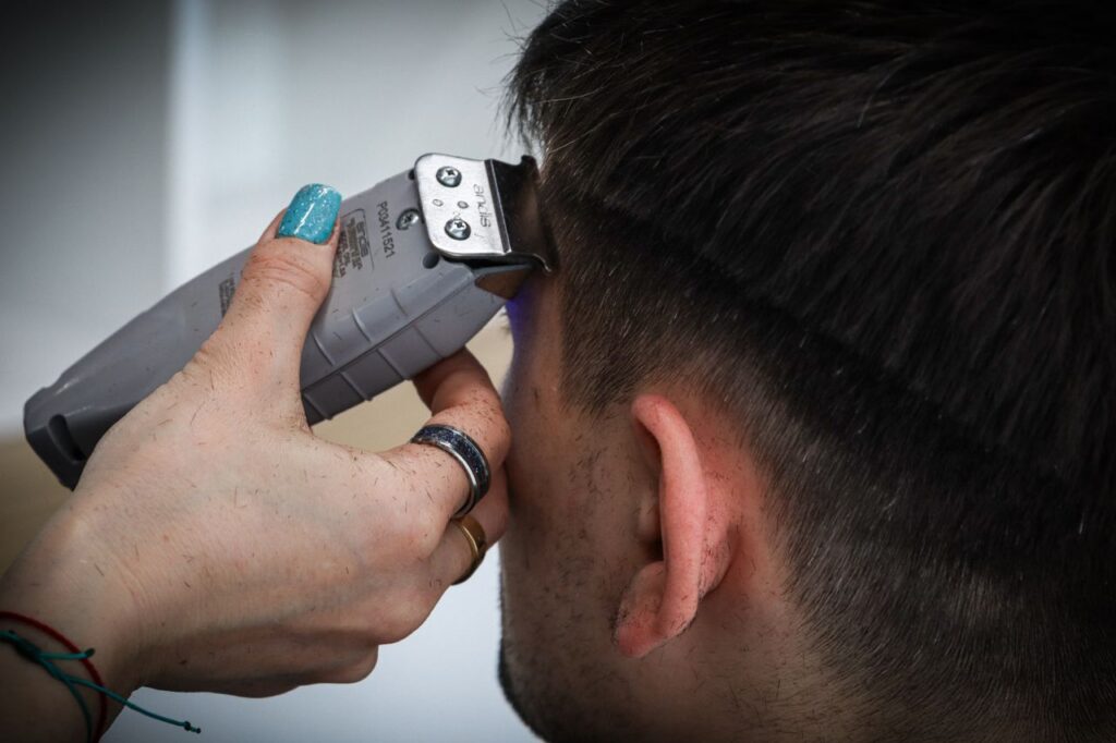 Detailed view of a haircut in progress with electric clippers and stylist's hand.