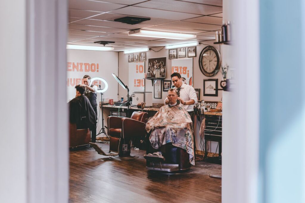 Professional barbers cutting hair of male clients sitting on chairs in traditional barbershop