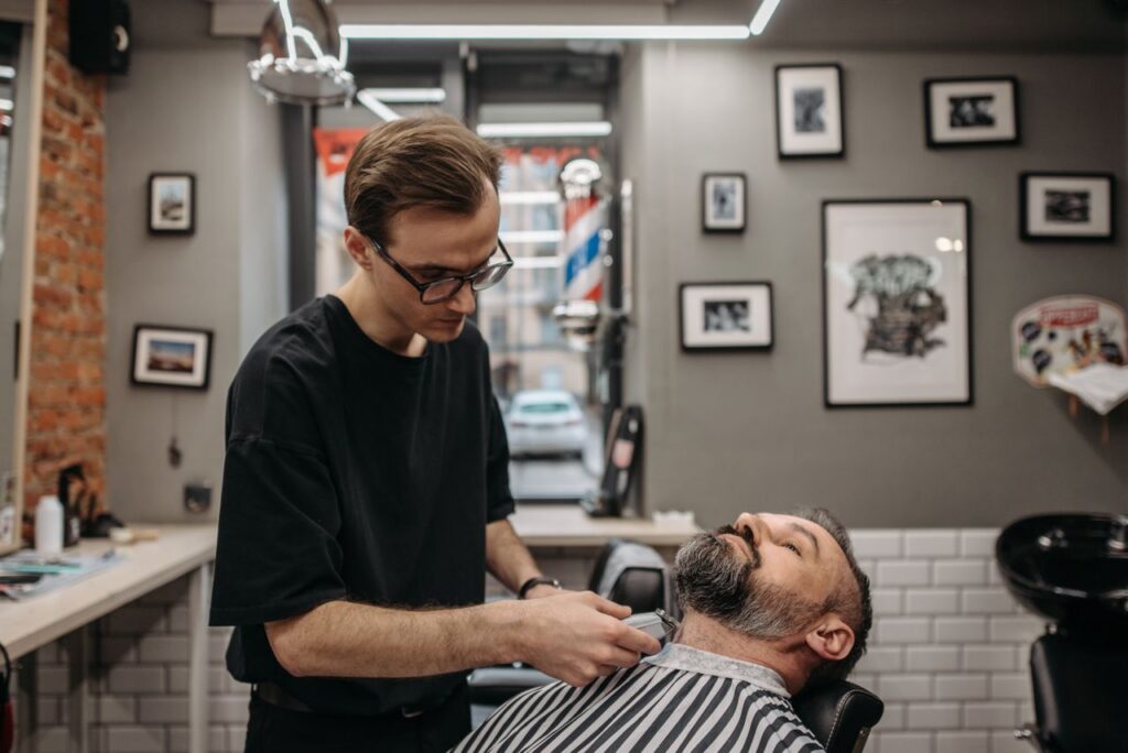 A barber meticulously trims a bearded man's hair in a contemporary barbershop setting.